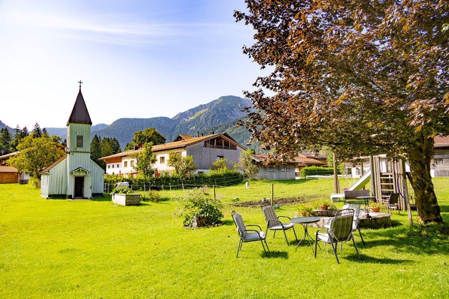 Gästegarten mit Liegen, dahinter Kirche und Berge