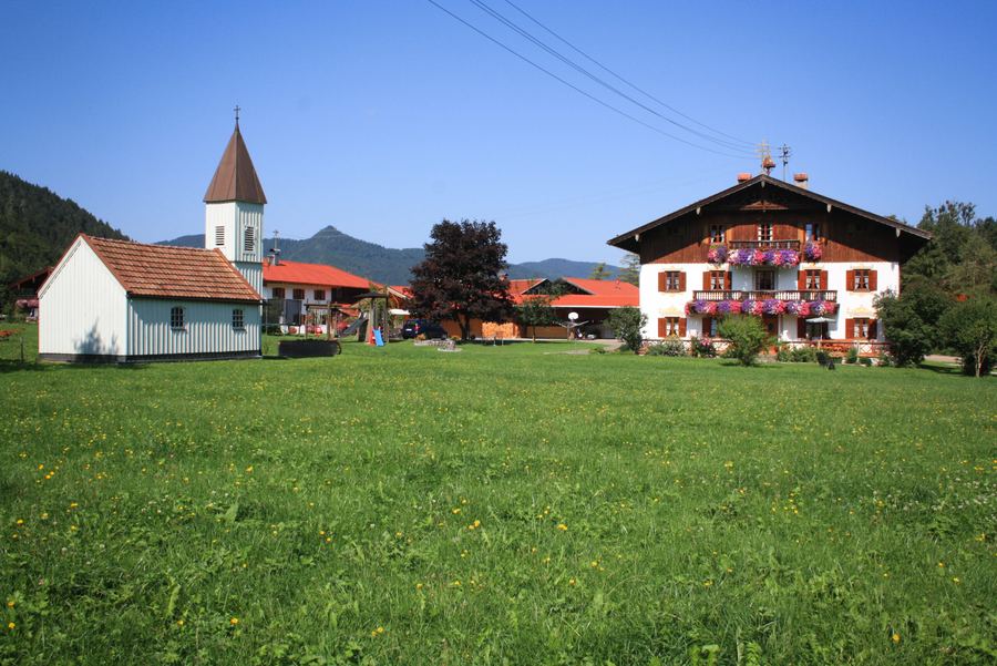 Kirche und Gödenbauernhof hinter einer grünen Wiese